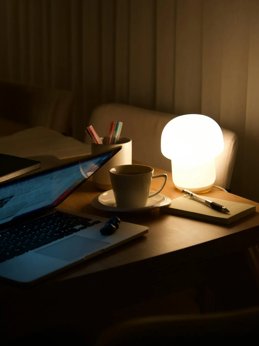 Warm evening workspace with an open laptop, lamp, and coffee on a tidy desk.