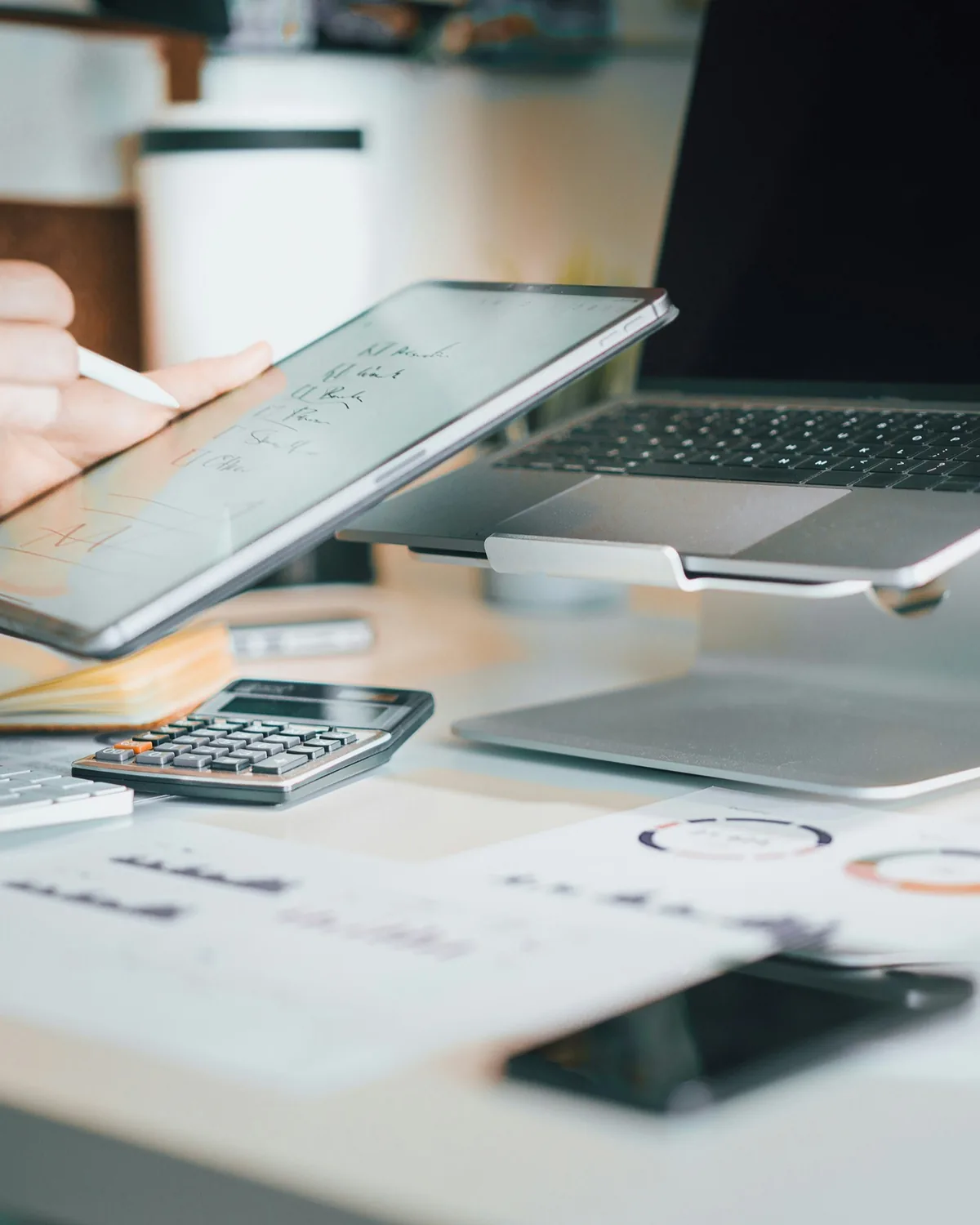 Working desk with a laptop, tablet, calculator, notebook, and financial charts.